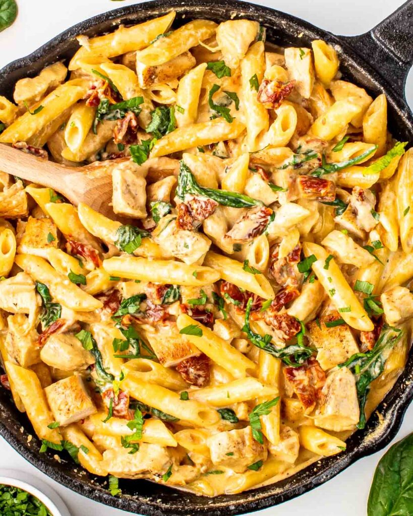 Creamy chicken penne pasta with spinach and sun-dried tomatoes in a skillet, garnished with fresh herbs.
