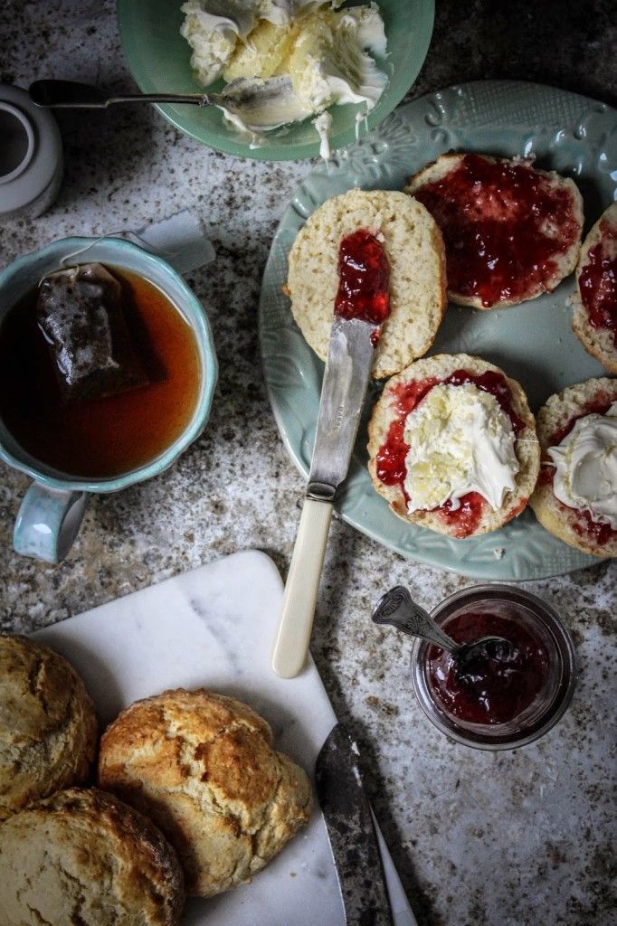 Tea time with scones, clotted cream, and jam, served on a rustic table alongside a cup of tea.