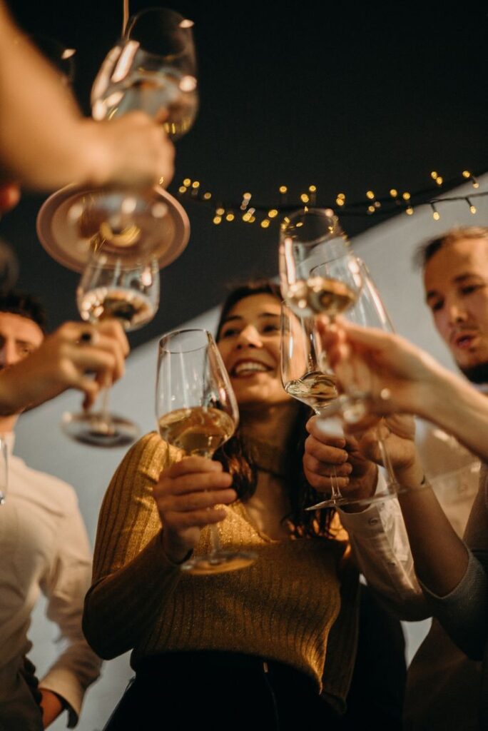 Group of friends toasting with wine glasses at a festive celebration under warm string lights.
