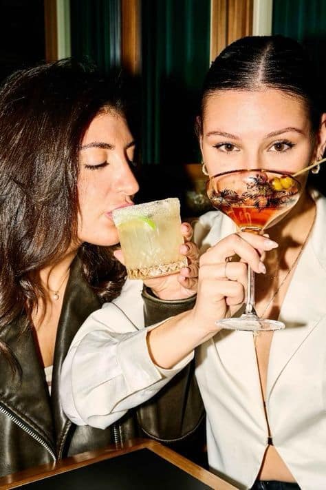 Two women enjoying colorful cocktails at a bar, capturing a fun and lively night out.