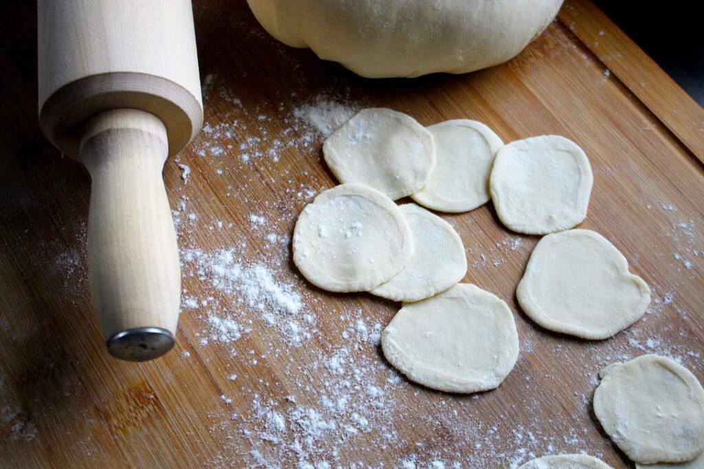 Rolling pin and dough circles on a floured board for homemade baking preparation.