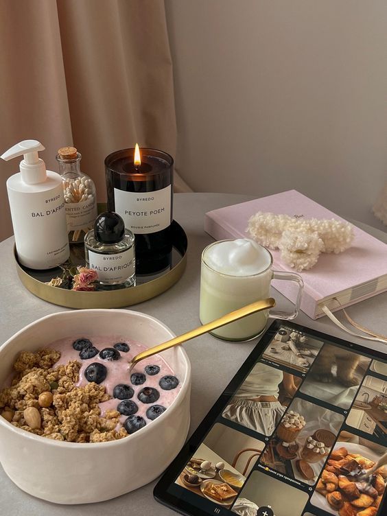Cozy morning scene with yogurt bowl, candle, coffee, and tablet on a table.