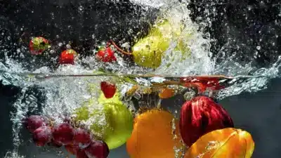 Fruits splashing in water, including strawberries, apple, grapes, and orange, creating a refreshing, vibrant effect.