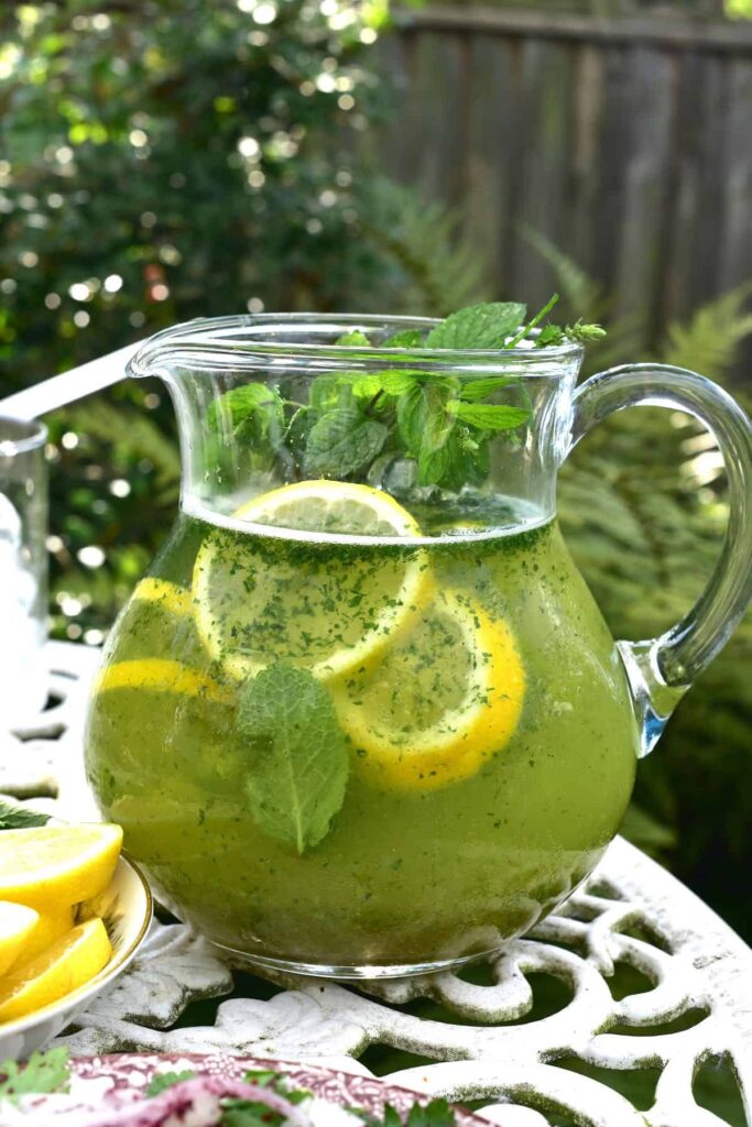 Pitcher of refreshing mint lemonade with lemon slices on a table outdoors.