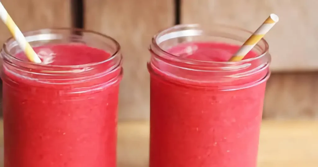 Two vibrant red smoothies in glass jars with striped straws, set against a wooden background. Refreshing and fruity.