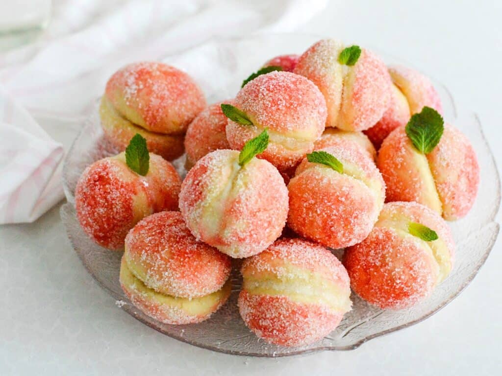 Sugared peach cookies with mint garnishes on a glass plate, perfect for dessert or a sweet treat.