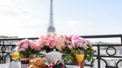Parisian breakfast with croissants, fruit, and flowers on a balcony overlooking the Eiffel Tower.