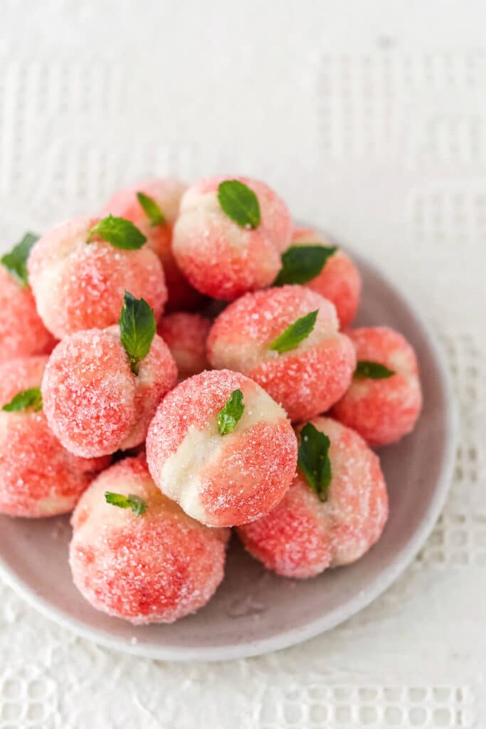 Plate of sugar-coated peach cookies with mint leaves, creating a refreshing and sweet dessert presentation.