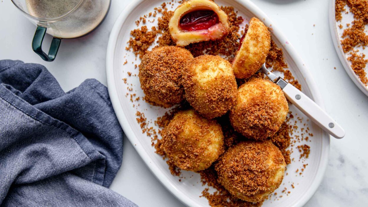 Plate of plum dumplings with breadcrumbs, a fork, and a cup of coffee on a marble surface.