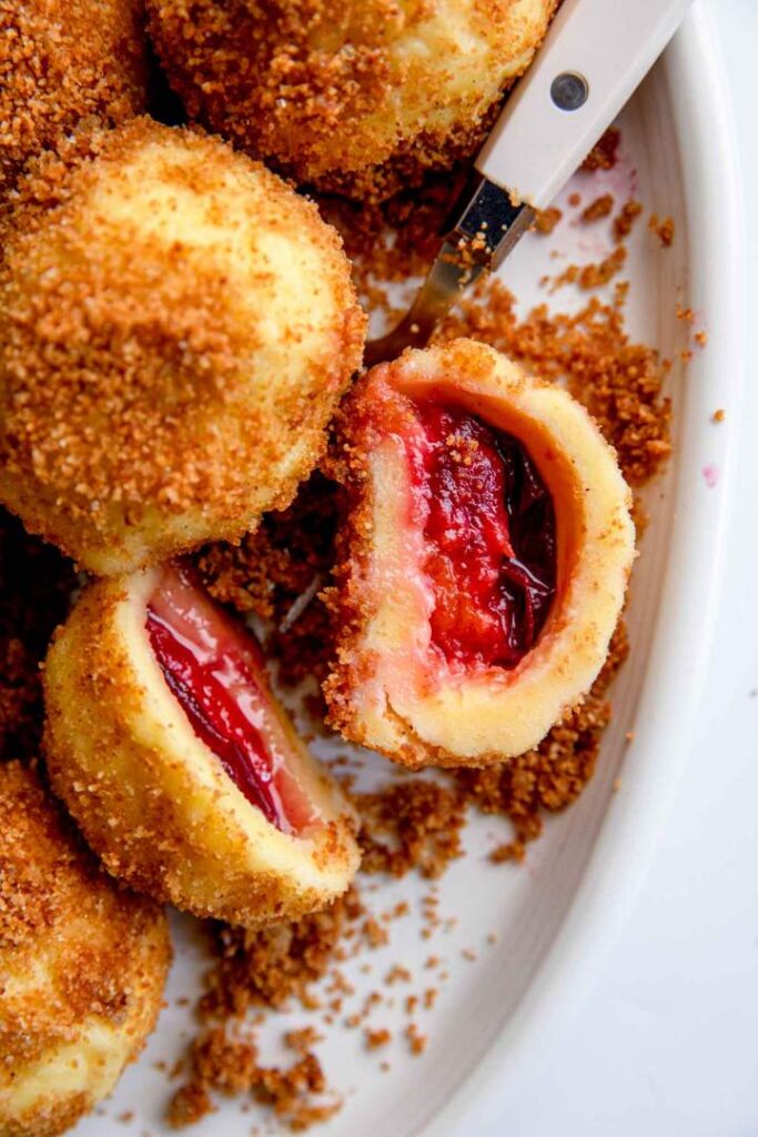 Plum dumplings with crispy breadcrumbs, sliced open to reveal juicy filling on a white plate. Perfect dessert treat.