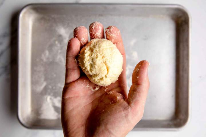 Person holding a ball of dough over a baking tray, ready for baking or cooking preparation.