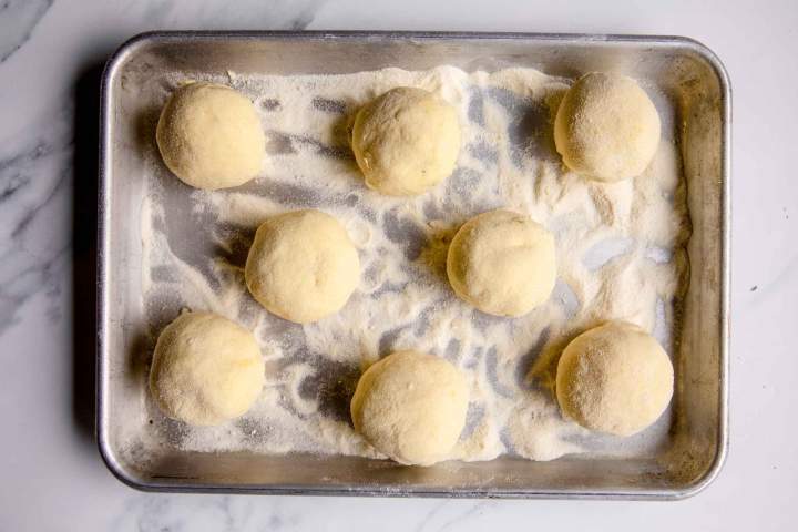 Eight round dough balls on a floured baking tray, ready for baking or cooking preparation.