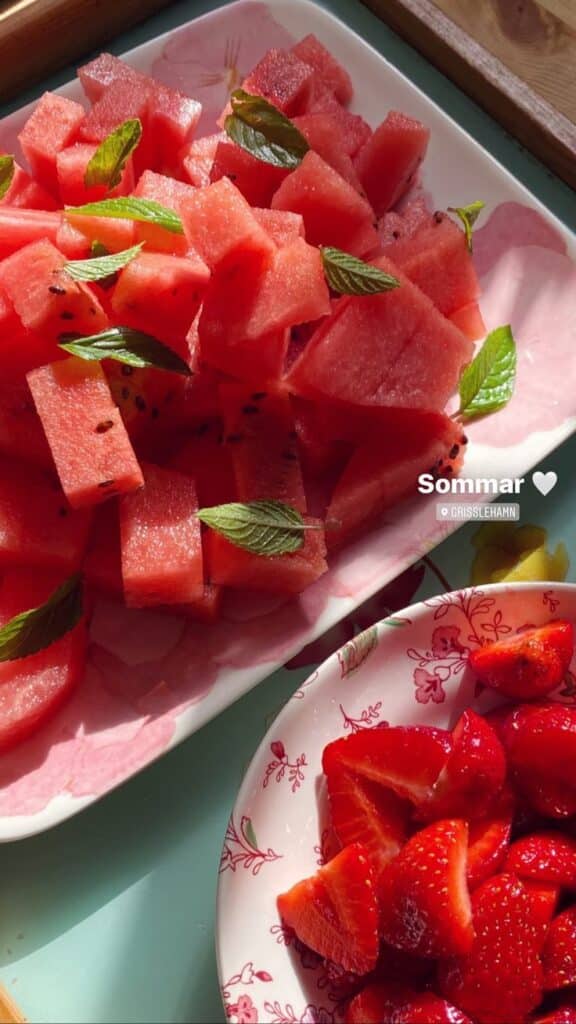 Fresh watermelon cubes with mint leaves and strawberries in bowls, perfect for a summer treat.