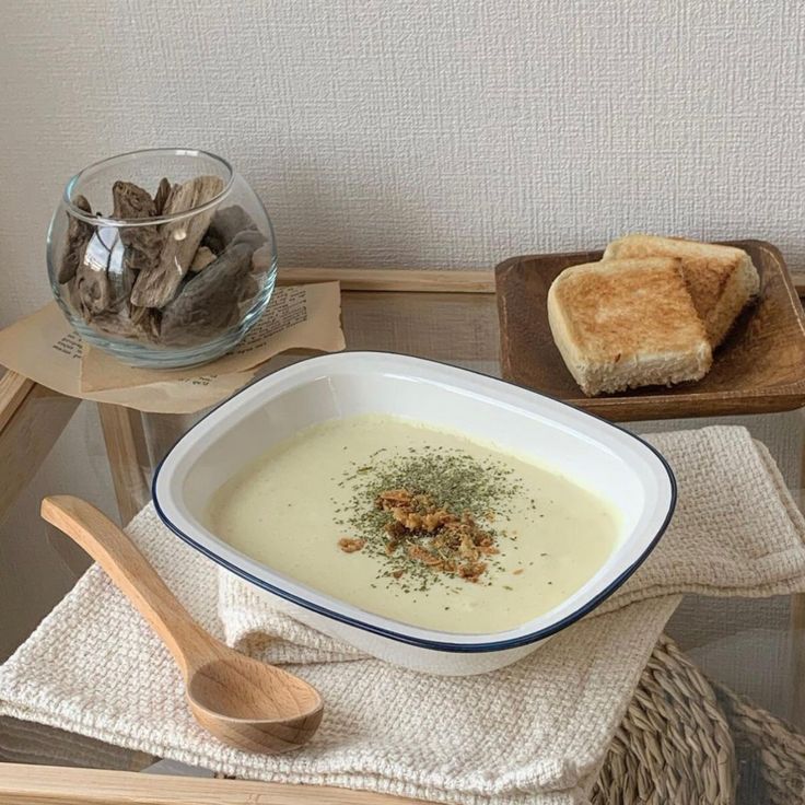 Creamy soup garnished with herbs and toasted bread on a wooden tray, beside a jar with decorative elements.