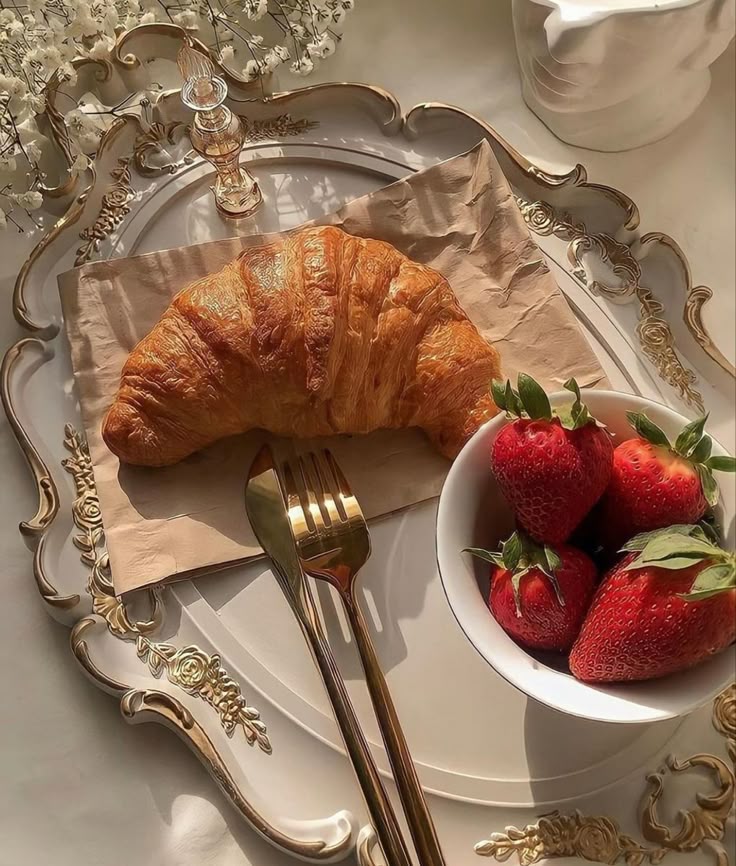 Golden croissant with fresh strawberries on an elegant plate, enhanced by warm sunlight and luxurious decor.