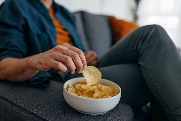 Person relaxing on a couch while enjoying a bowl of potato chips.