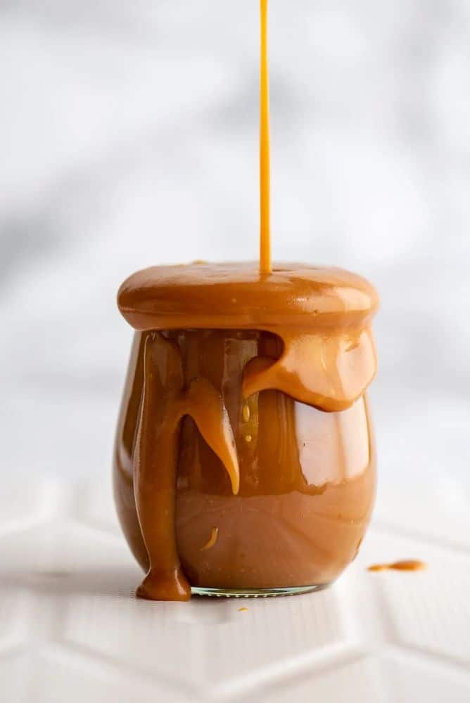 Smooth caramel sauce dripping from a jar, creating a delicious, mouthwatering visual on a white background.