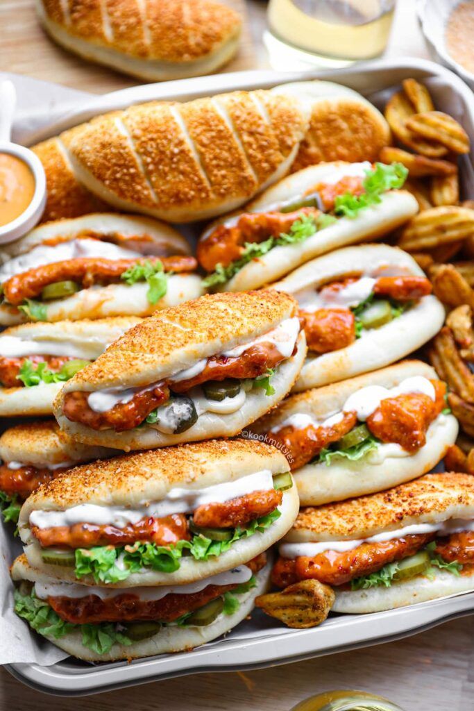 A tray of spicy chicken sandwiches with lettuce, sauce, and pickles, alongside seasoned potato wedges, perfect for lunch.