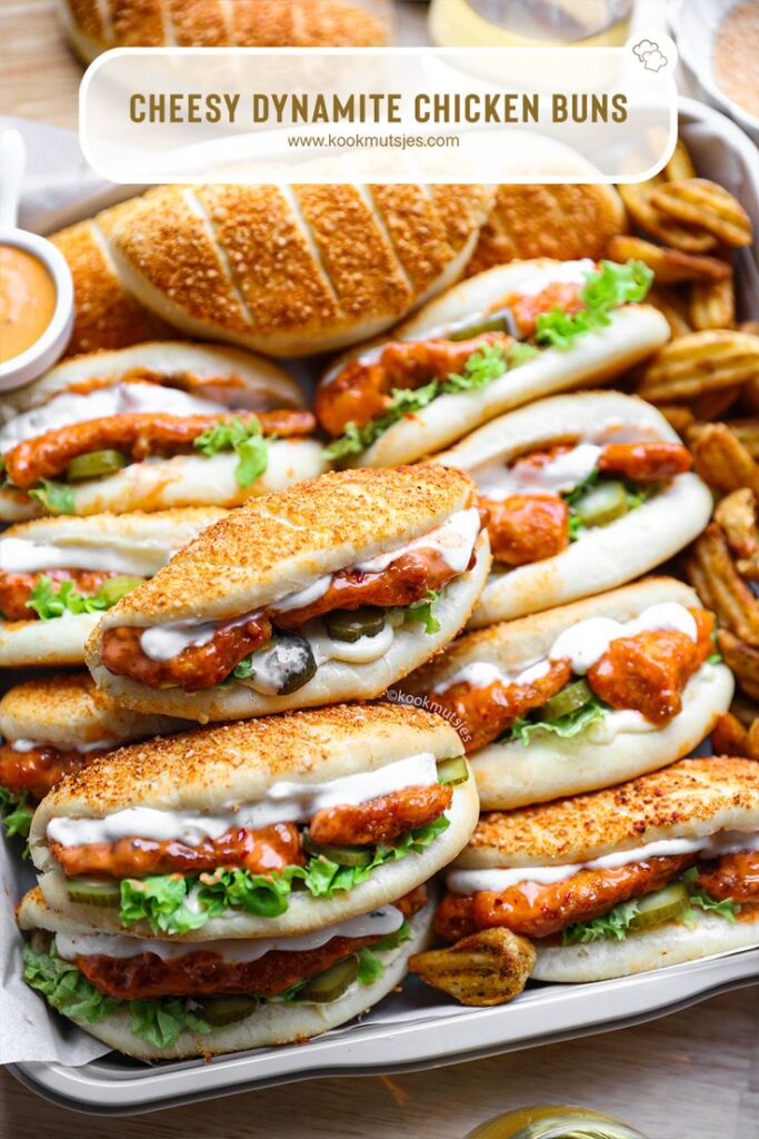 Cheesy dynamite chicken buns with spicy sauce, lettuce, and pickles on a tray. Perfect for a tasty snack.