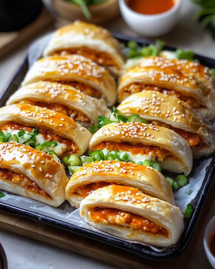 Flaky pastries filled with spicy buffalo chicken, topped with sesame seeds and garnished with fresh green onions.