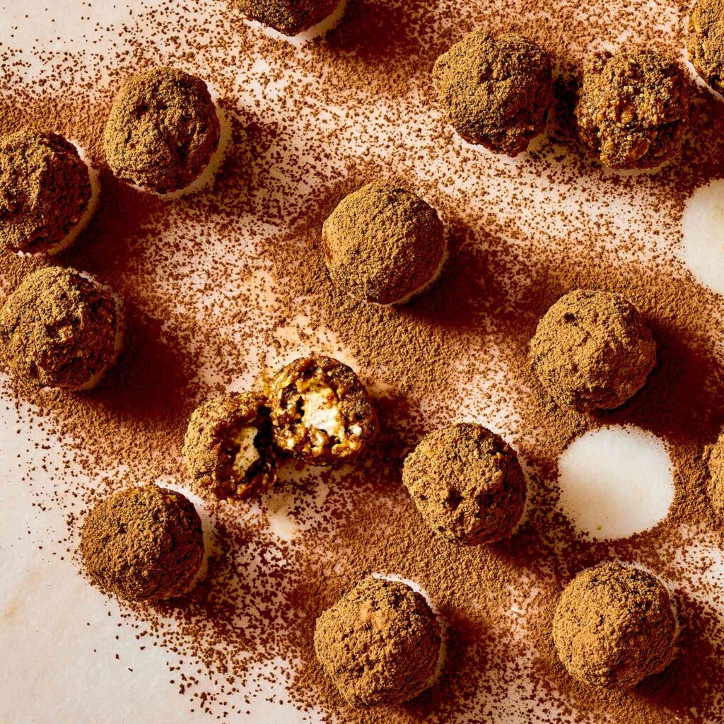 Chocolate truffles dusted with cocoa on a white surface, one cut open to reveal creamy filling.