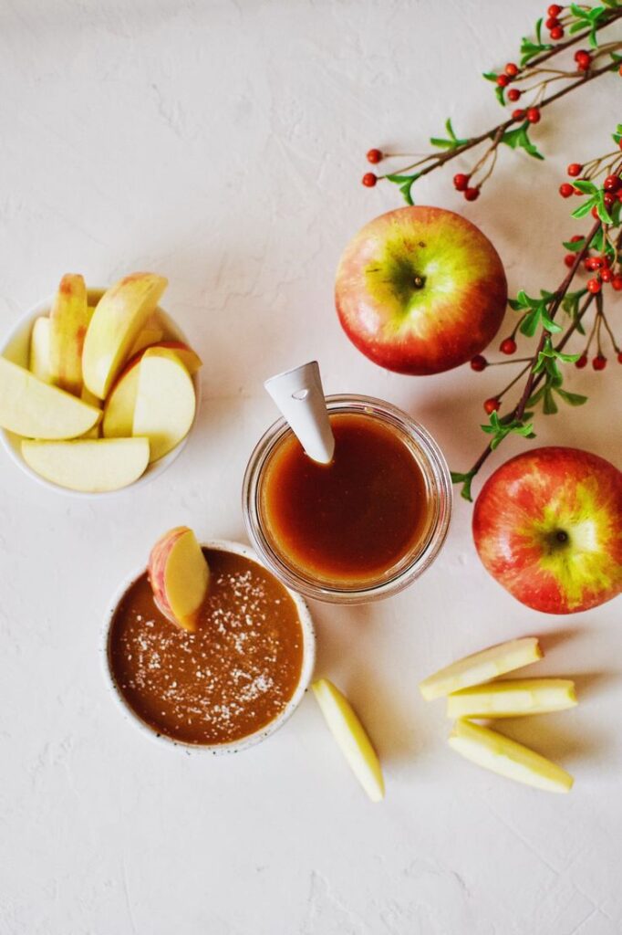 Sliced apples with caramel dip and fresh apples on a white background, garnished with festive berries.