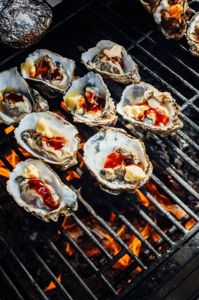 Grilled oysters topped with butter and sauce on a barbecue grill with flames below, creating a delicious seafood dish.