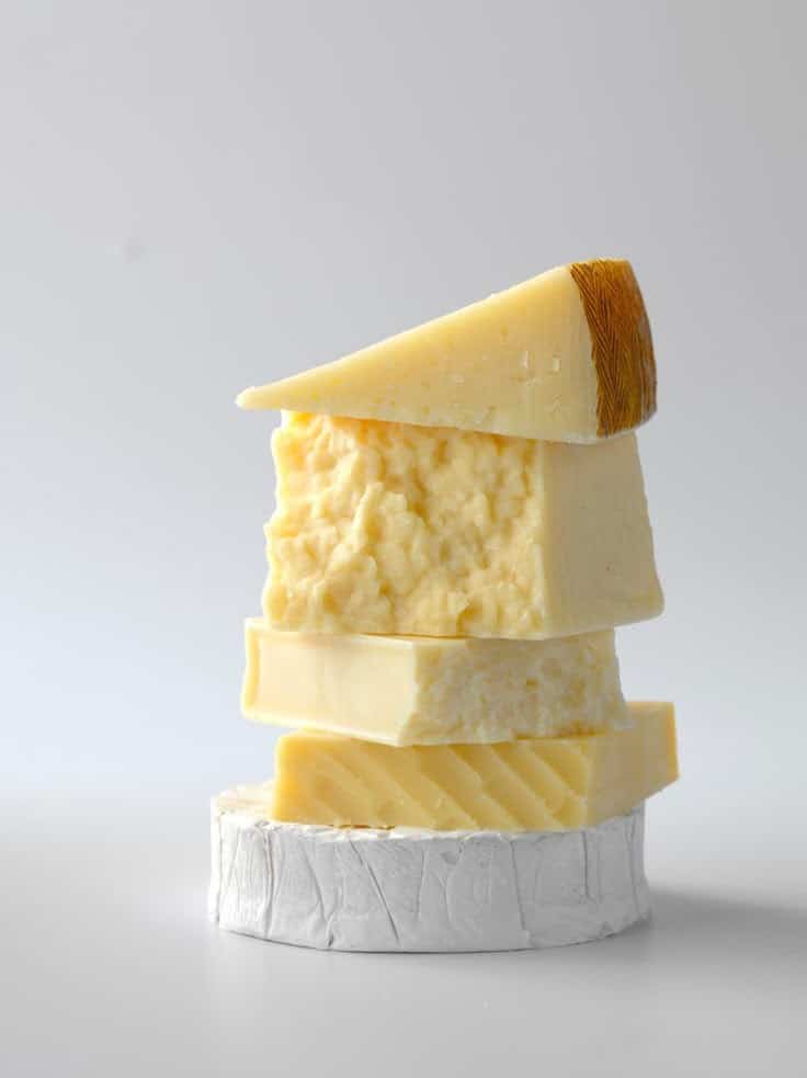Stack of assorted cheeses on a plain background, showcasing various textures and types. Perfect for gourmet food enthusiasts.