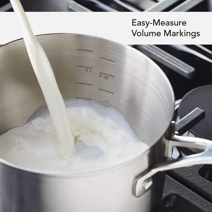 Pouring milk into a stainless steel pot with easy-measure volume markings on a stove.