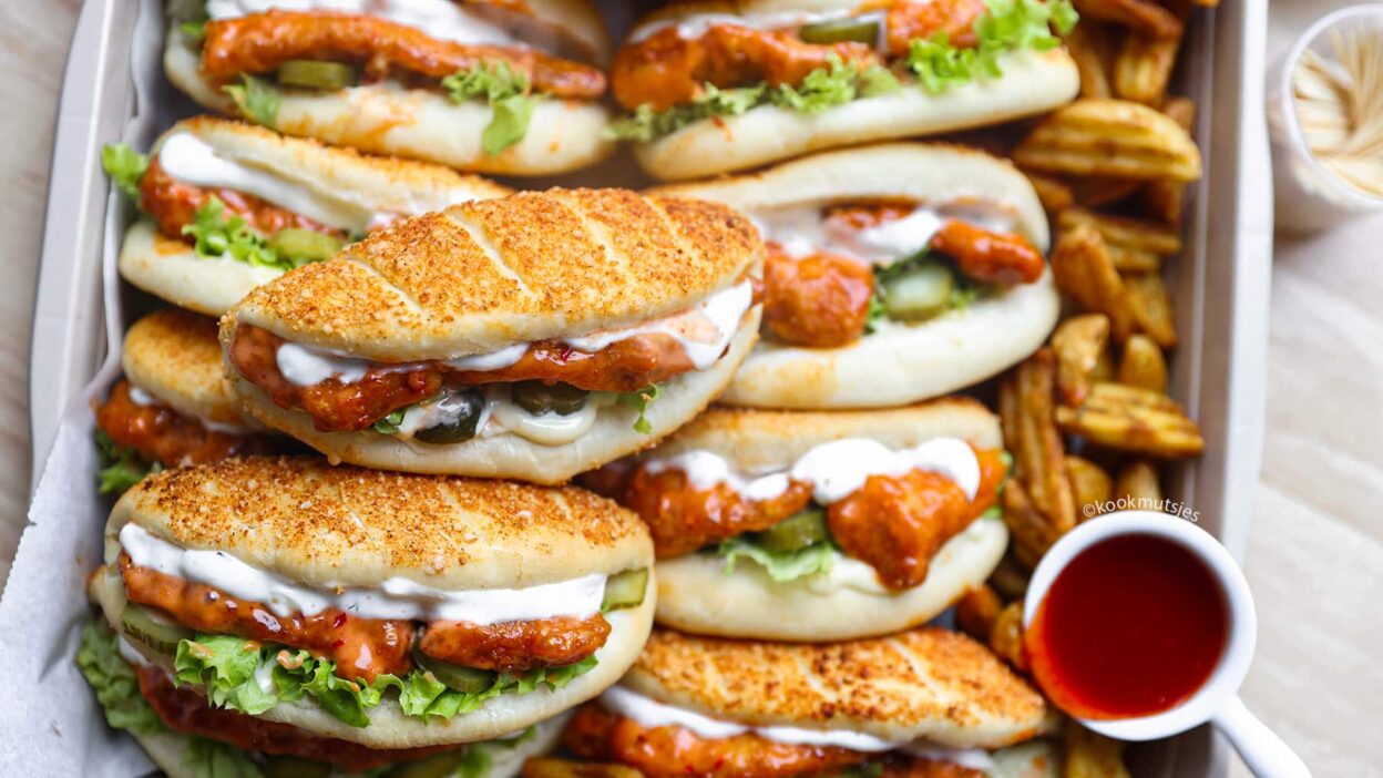 Delicious spicy chicken sandwiches with lettuce, pickles, and creamy sauce, served on a tray with potato wedges.