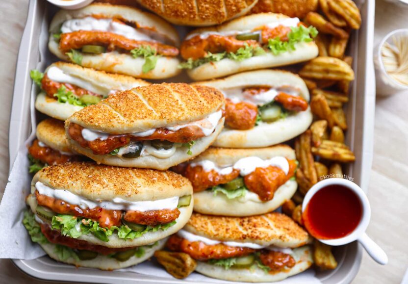 Delicious spicy chicken sandwiches with lettuce, pickles, and creamy sauce, served on a tray with potato wedges.