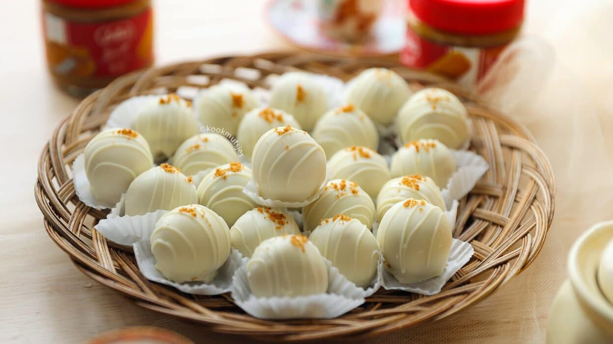 Basket of white chocolate truffles with sprinkles, jars and a cup in the blurred background.