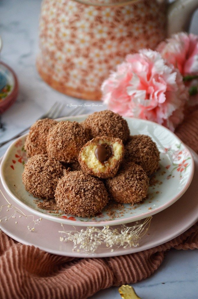 Plate of chocolate-filled coconut balls with a teapot and pink flowers in the background.