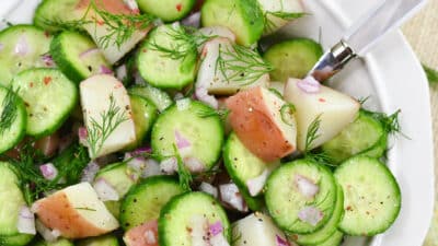 Fresh cucumber and potato salad with red onions and dill in a white bowl.