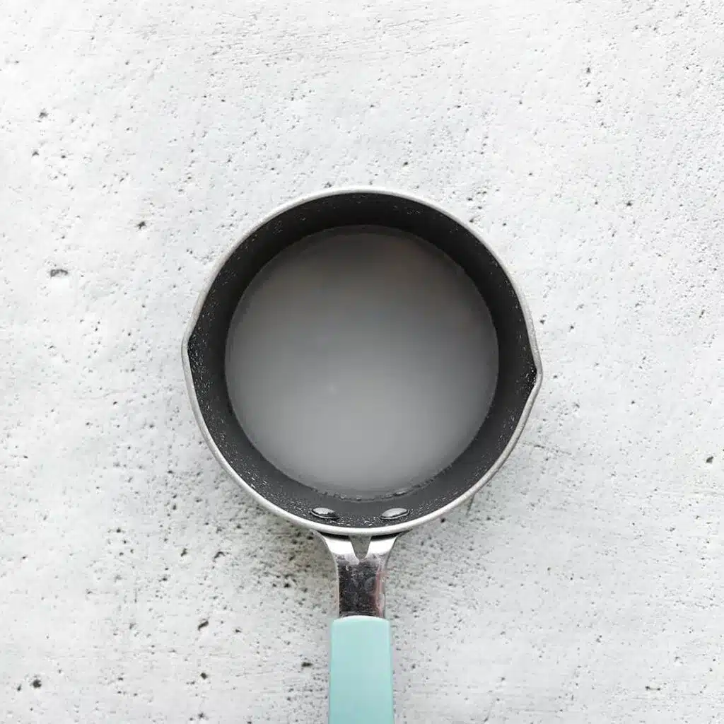 Small pot with white liquid on a textured gray surface, featuring a light blue handle. Cooking and kitchenware concept.