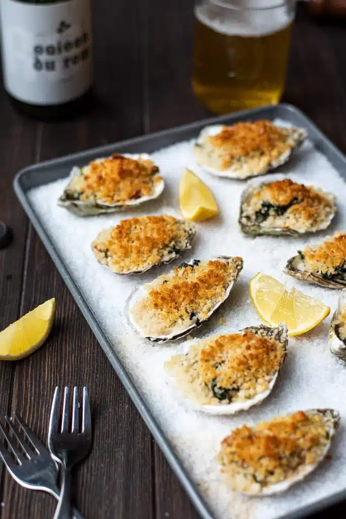 Baked oysters topped with golden breadcrumbs, served with lemon wedges on a tray.