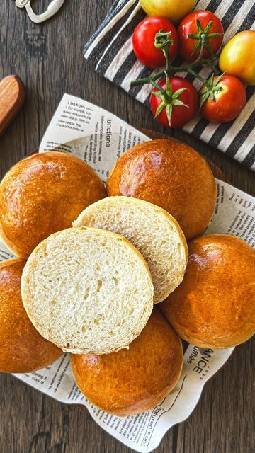 Golden brown bread rolls on newspaper-lined plate with fresh tomatoes on a striped cloth in the background.