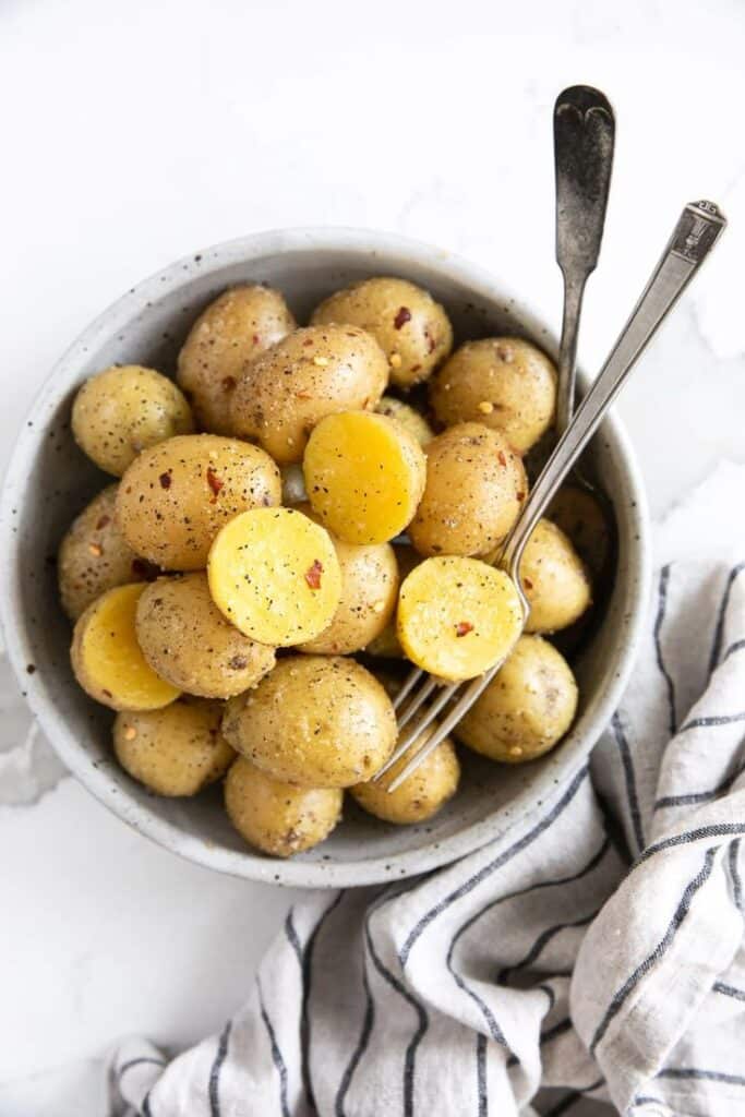 Bowl of seasoned boiled potatoes with forks and striped napkin on marble surface.