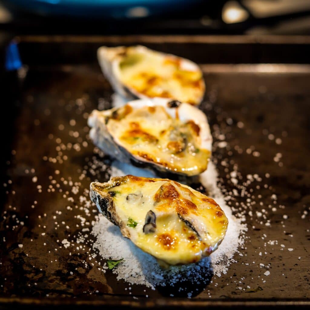Baked oysters with melted cheese and herbs on a tray with sea salt. Perfect seafood appetizer for gourmet meals.