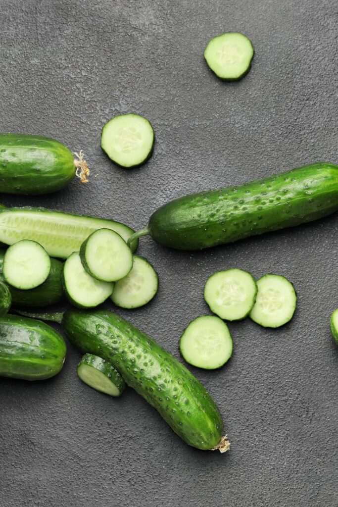 Fresh whole and sliced cucumbers on a dark surface, showcasing green textures and vibrant colors.
