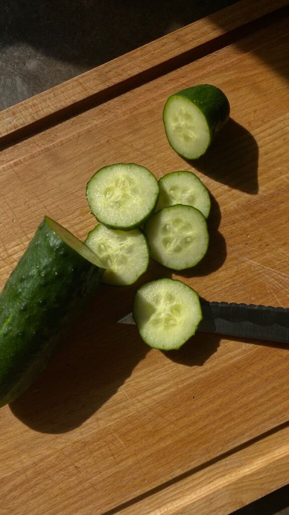 Fresh cucumber slices on a wooden cutting board with a serrated knife nearby.