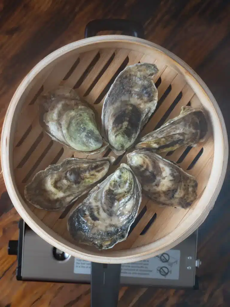 Steamed oysters in a bamboo steamer on a wooden table, ready for cooking.