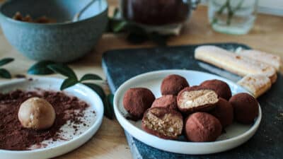 Homemade chocolate truffles on a plate, dusted with cocoa powder, with a truffle in preparation in the background.
