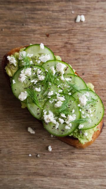 Open-faced sandwich with cucumber slices, avocado spread, dill, and crumbled feta on rustic bread.