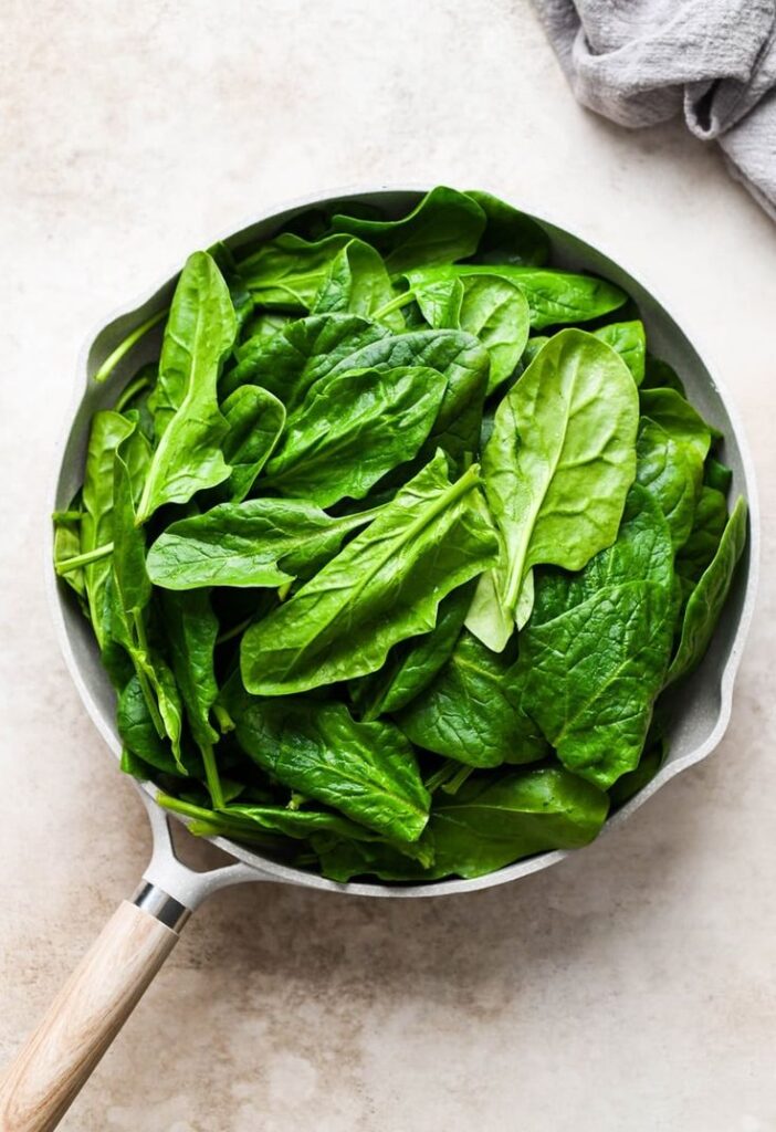 Fresh spinach leaves in a pan on a light countertop, ready for cooking. Healthy green vegetable preparation.