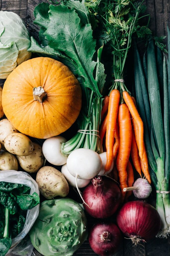 Assorted fresh vegetables: pumpkin, carrots, onions, potatoes, cabbage, and greens on a wooden background.