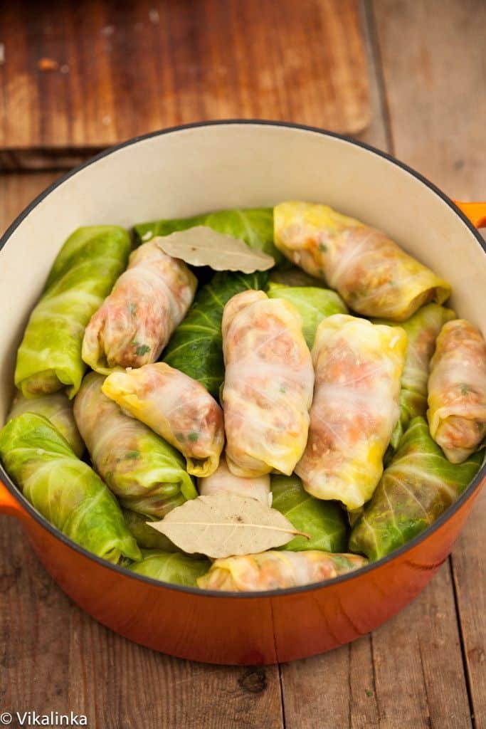 Pot filled with freshly cooked cabbage rolls, garnished with a bay leaf, on a wooden table.