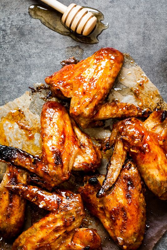 Honey-glazed chicken wings on parchment with a honey dipper, showcasing golden, crispy perfection.