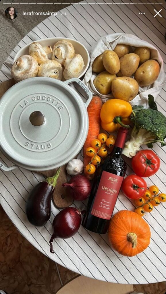 Colorful vegetables, wine, and a Staub pot on a striped tablecloth, perfect for a cozy cooking session.