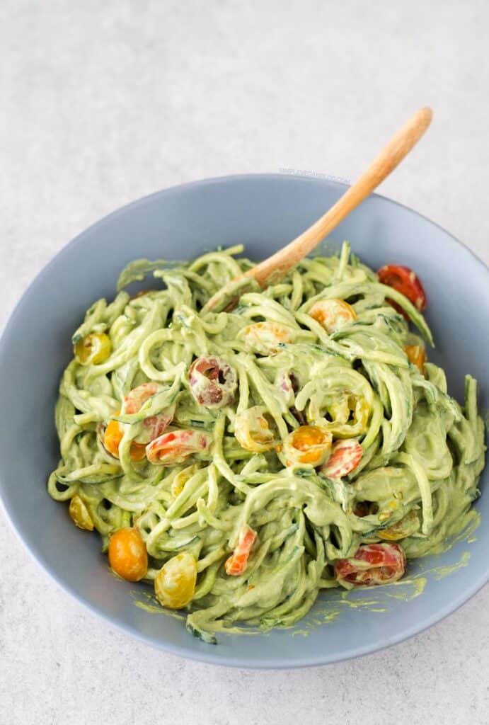 Creamy zucchini noodles with avocado sauce and cherry tomatoes in a blue bowl. Perfect for a vegan meal.